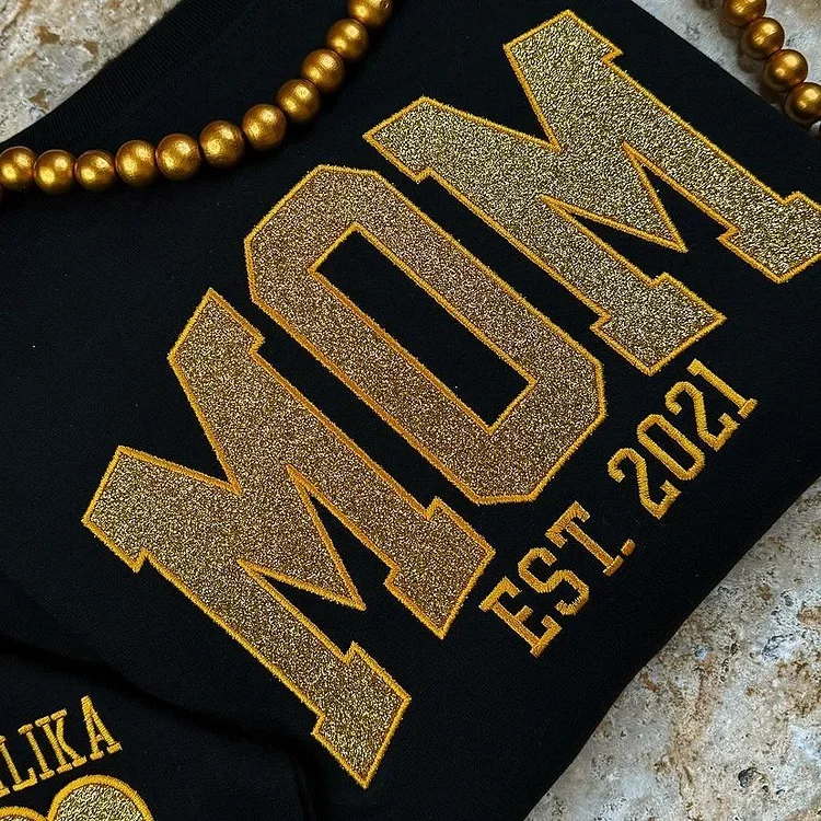 Close-up of the delicate glitter-embroidered children's names on the sleeve of a cozy mom sweatshirt.